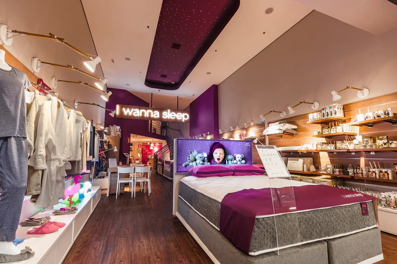 Interior de uma loja física da I Wanna Sleep, com letreiro luminoso da marca e cama de exposição