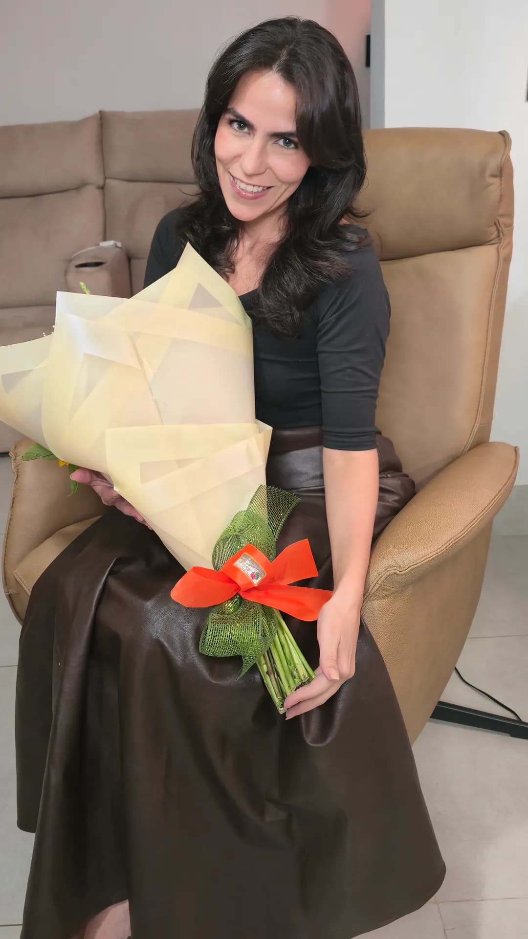 Cecília sentada na Poltrona Levita ao lado de um arranjo de flores.